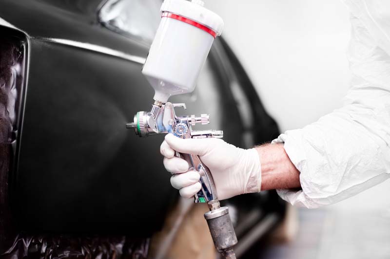 Close-up of worker using a paint spray gun to paint a car