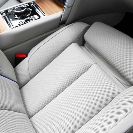 Modern luxury car white leather interior with natural wood panel. Part of leather car seat details with stitching. Interior of prestige modern car. White perforated leather. Car detailing. Car inside